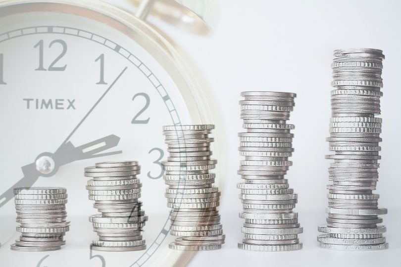 A growing stack of coins over a stopwatch, indicating revenue growth over time