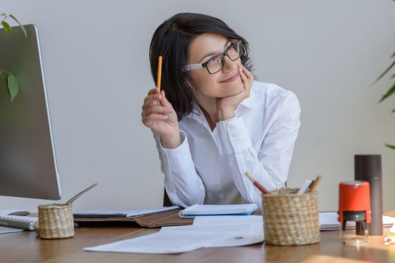 Happy woman thinking at her desk