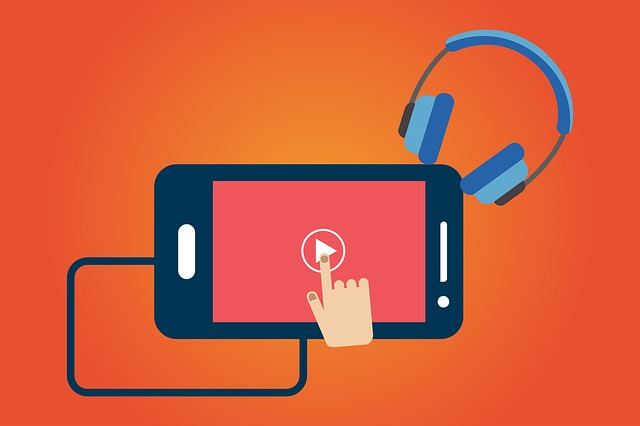 A hand clicks play on a video on a smartphone; headphones rest beside it.