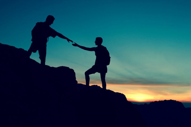 Climbers helping each other ascend a mountain.