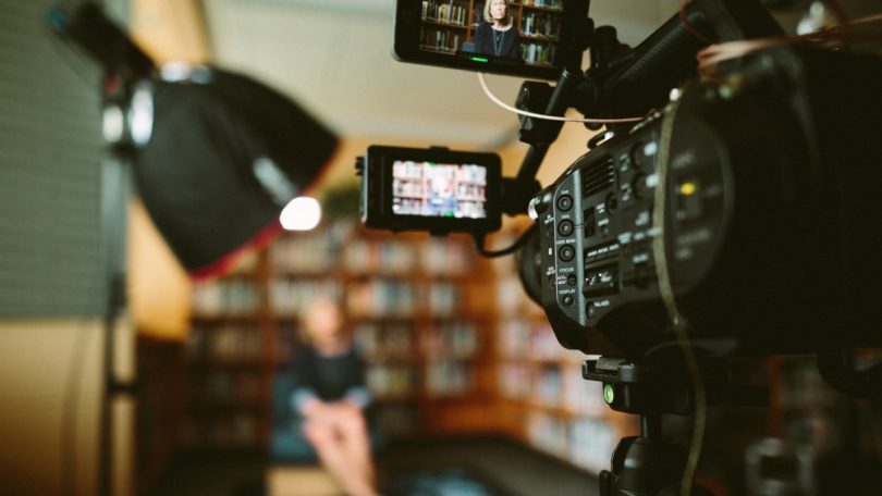 A camera livestreaming a woman giving a presentation in a library