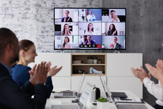 A group of people applauding a live stream they're watching on the conference room monitor.