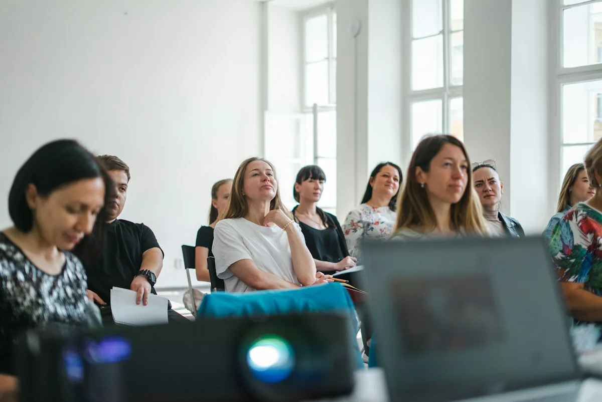 Adults taking notes and listening during a professional workshop in a sunlit room.