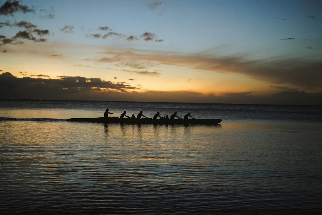 A rowing team moving together across calm water at sunset.