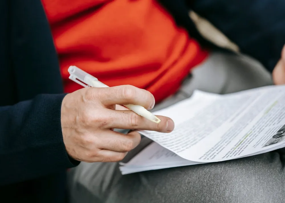 A person using a pen to review highlighted printed material outdoors.