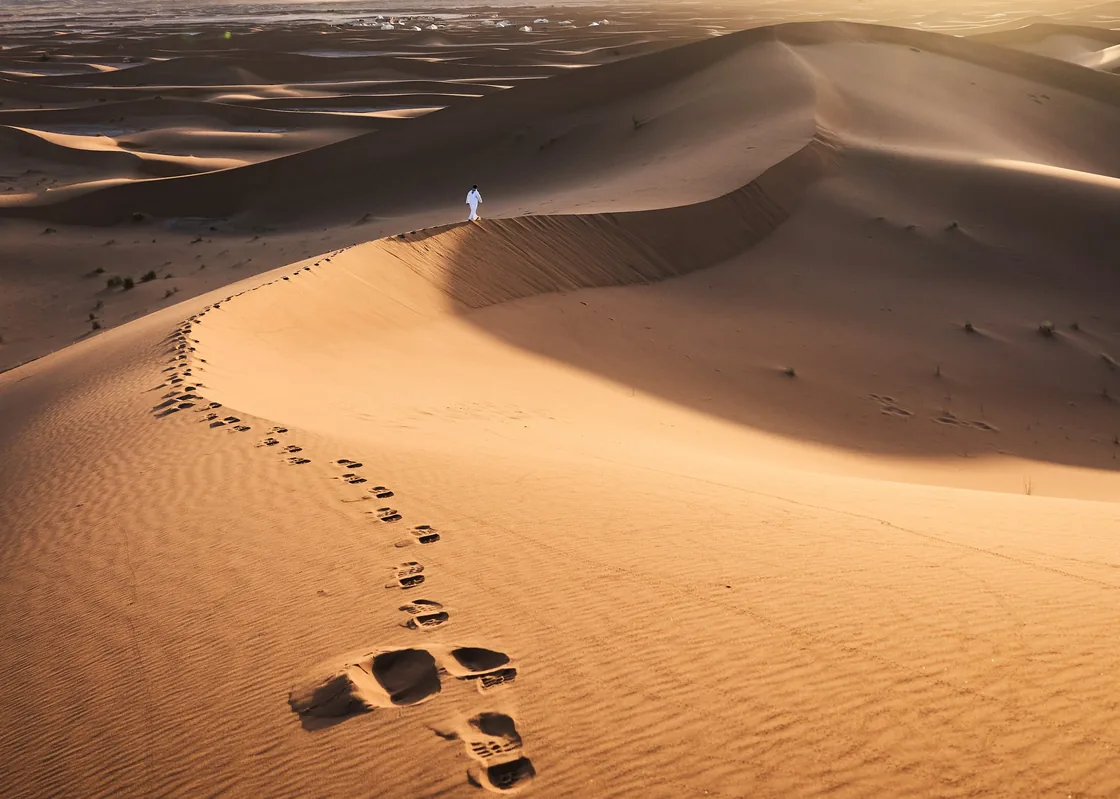Footprints tracing a route across warmly lit sand dunes.