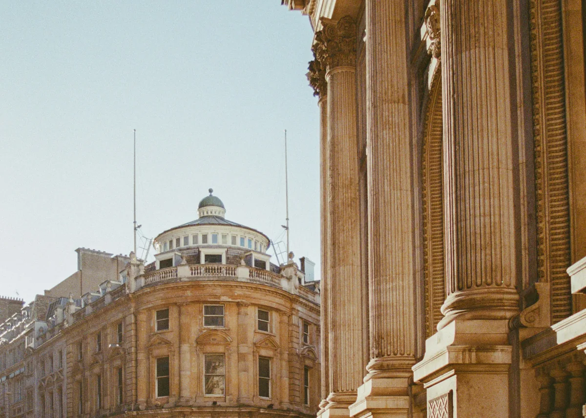 People walk beside grand columns in warm sunlight.