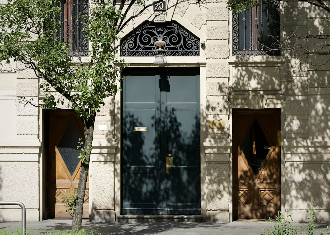 Sunlit entrance with three open doors and tree shadows.