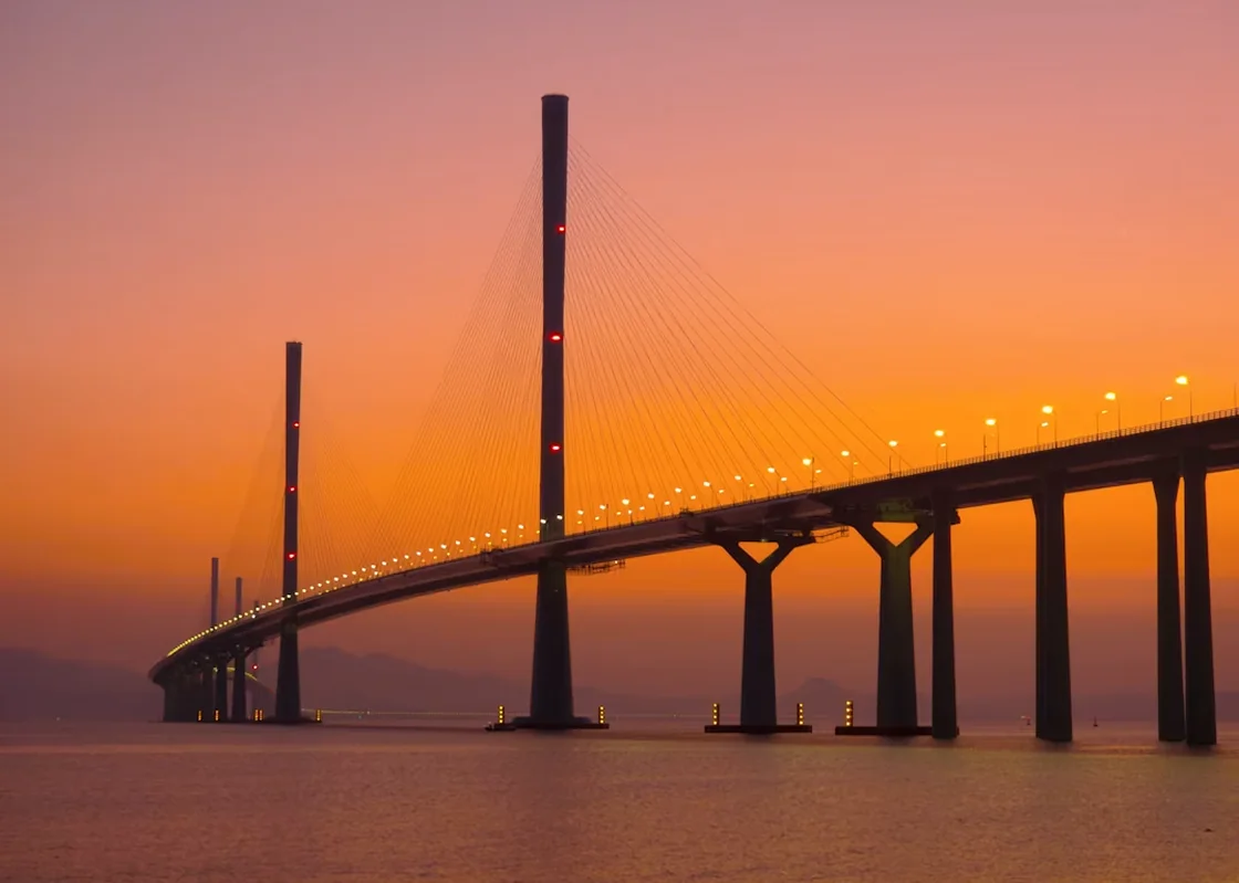 Modern suspension bridge glowing at sunset over calm water.