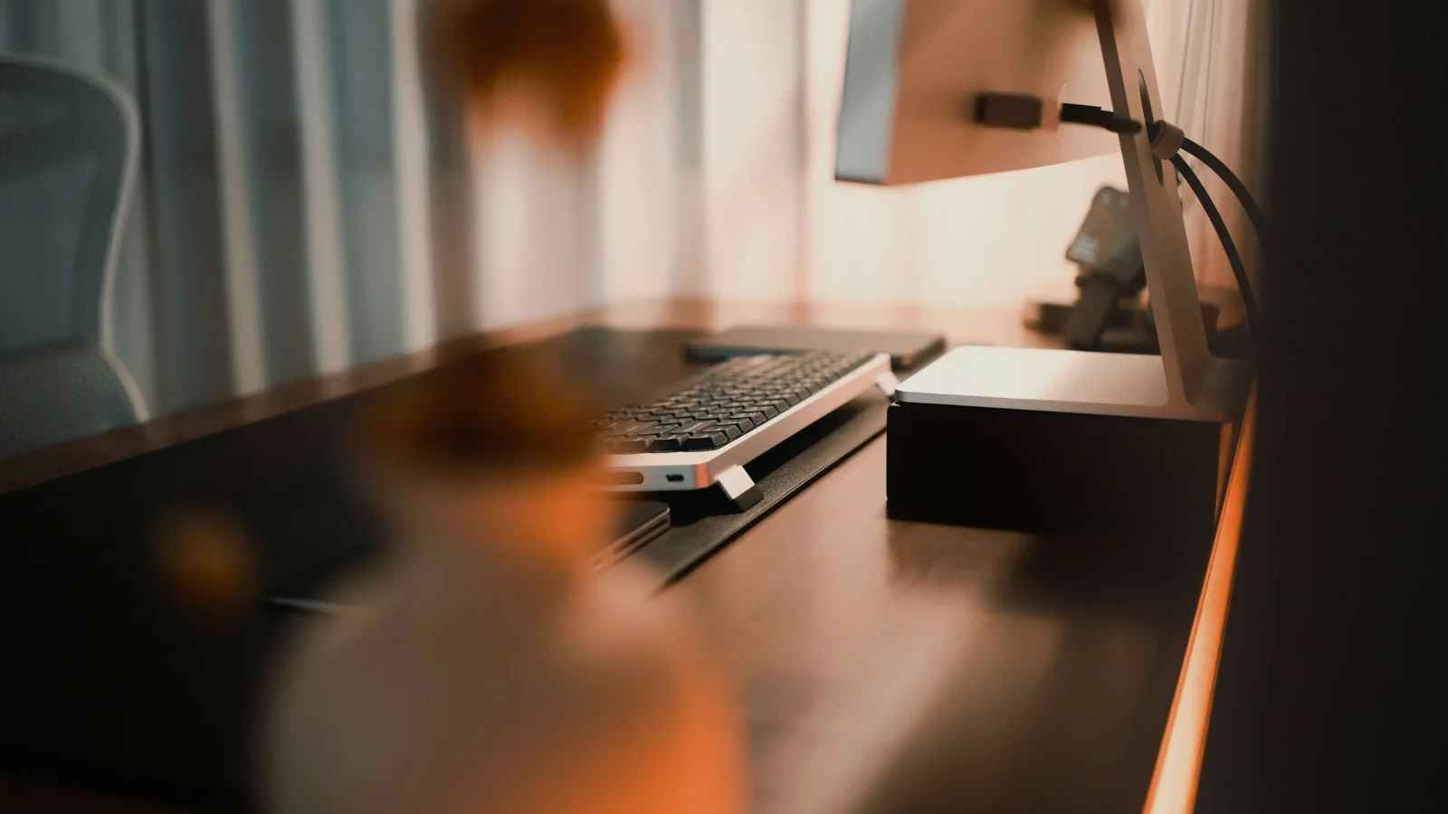 Warmly lit home office desk with laptop, keyboard and monitor.