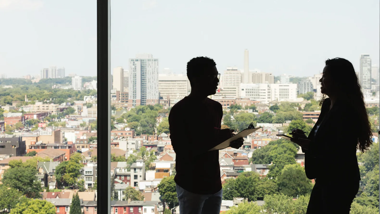 Two colleagues exchanging working knowledge beside a sunlit office window.