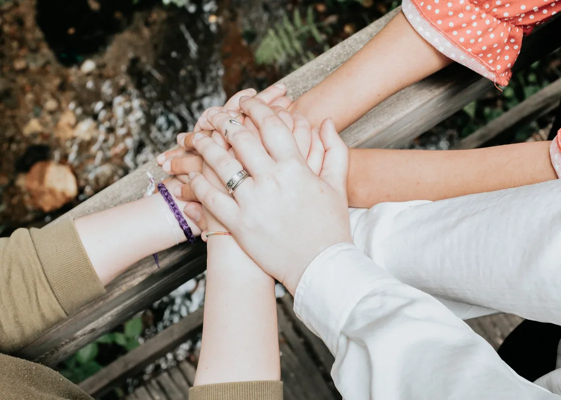 Hands resting together on a wooden railing in a natural setting.